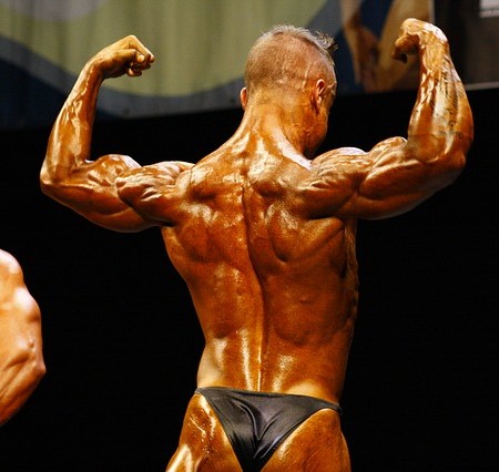 A greased up, tanned, male bodybuilder wearing a thong