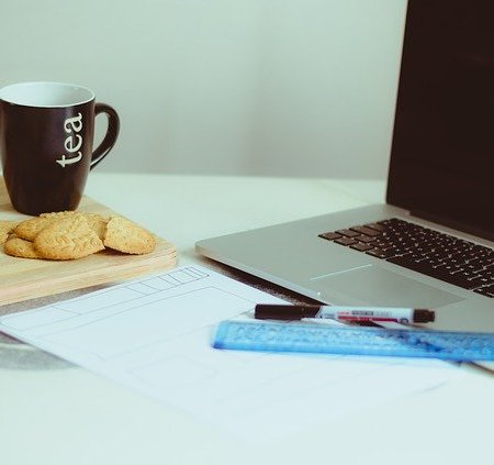 A cup of tea with some biscuit to dunk, next to a laptop