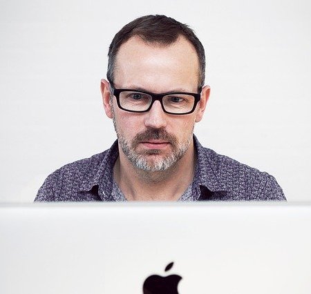 A Reply Guy sitting behind his Apple Mac computer.
