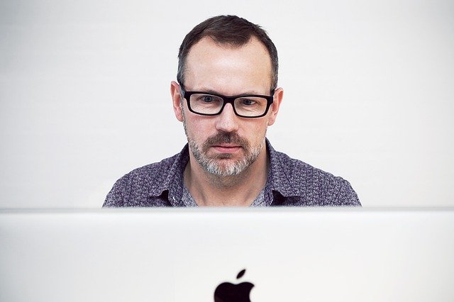 A Reply Guy sitting behind his Apple Mac computer.