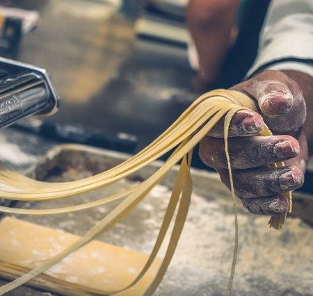 A man holding strings of fresh pasta.