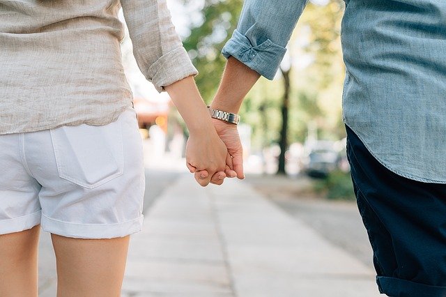 A couple holding hands in public on a sunny day.