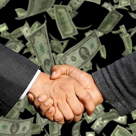 Two businessmen shaking hands to the backdrop of money.
