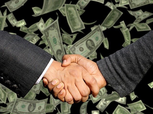 Two businessmen shaking hands to the backdrop of money.