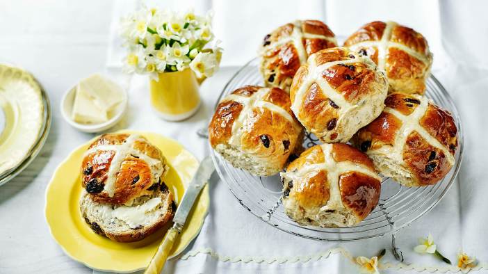 A selection of hot cross buns, one of which is on a yellow plate.