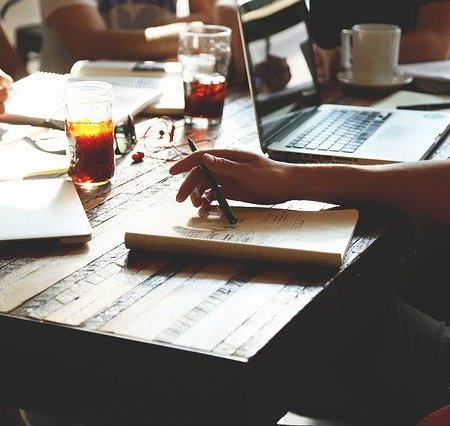 A business working at a table with people writing and drinks nearby