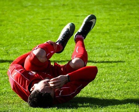 A footballer rolling on the pitch in pain clutching his kneecap