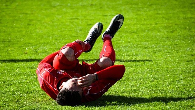 A footballer rolling on the pitch in pain clutching his kneecap