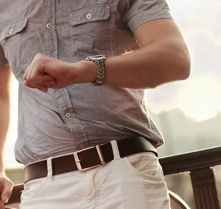 A man looking at his watch realising it's time to take his top off