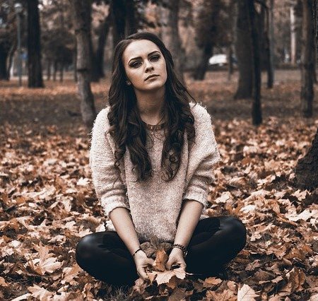An upset girlfriend sitting on some autumn leaves